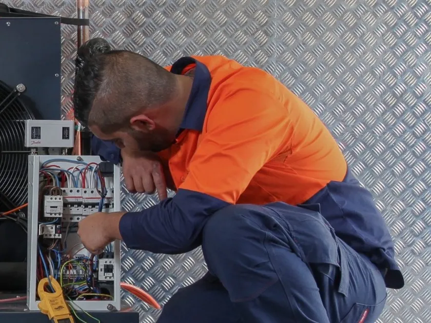 A refrigeration technician working on the electrical control panel of a commercial refrigeration unit
